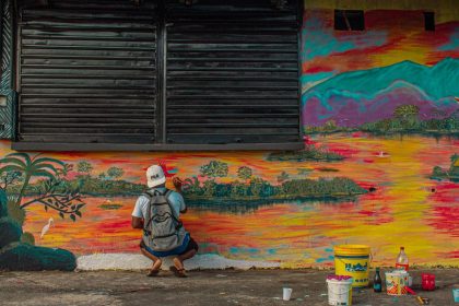 Artista pinta um mural colorido ao ar livre, em uma cena de produção cultural.
