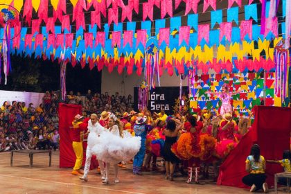 Dançarinos participam de uma celebração brasileira colorida, cercados por enfeites festivos.