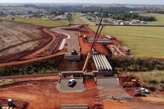 Vista aérea de uma obra de construção rodoviária, com máquinas trabalhando em meio à paisagem.