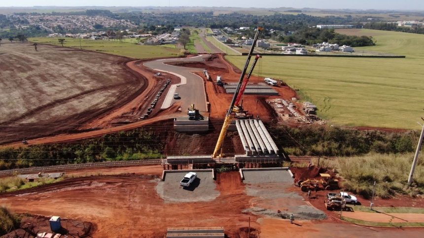 Vista aérea de uma obra de construção rodoviária, com máquinas trabalhando em meio à paisagem.